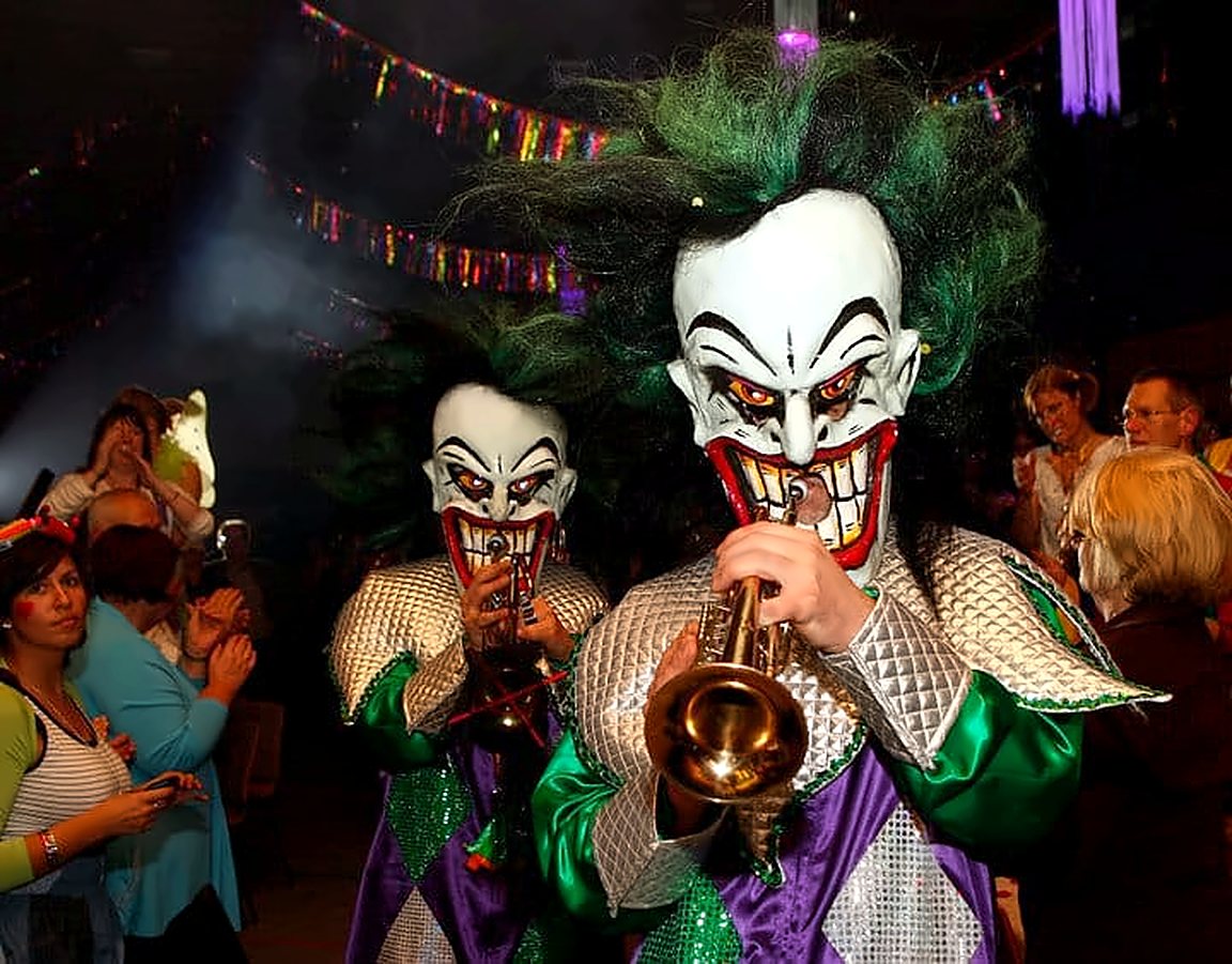 Joker-Maske mit grünen Haaren im Rautenkostüm spielt Trompete im Saal