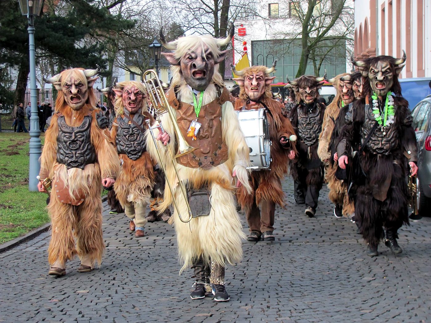 Die Lärmer mit gehörnten Fellmasken und Instrumenten beim Umzug auf einer gepflasterten Straße